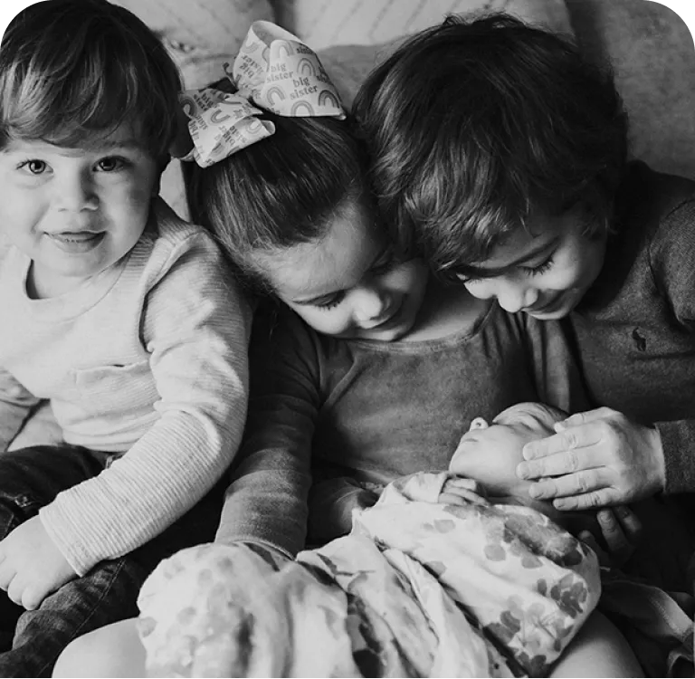Siblings leaning over a newborn